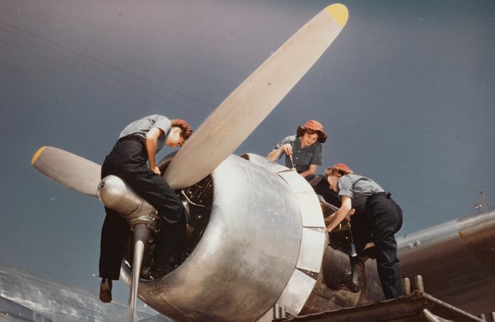 Three women working on the engine of an aeroplane